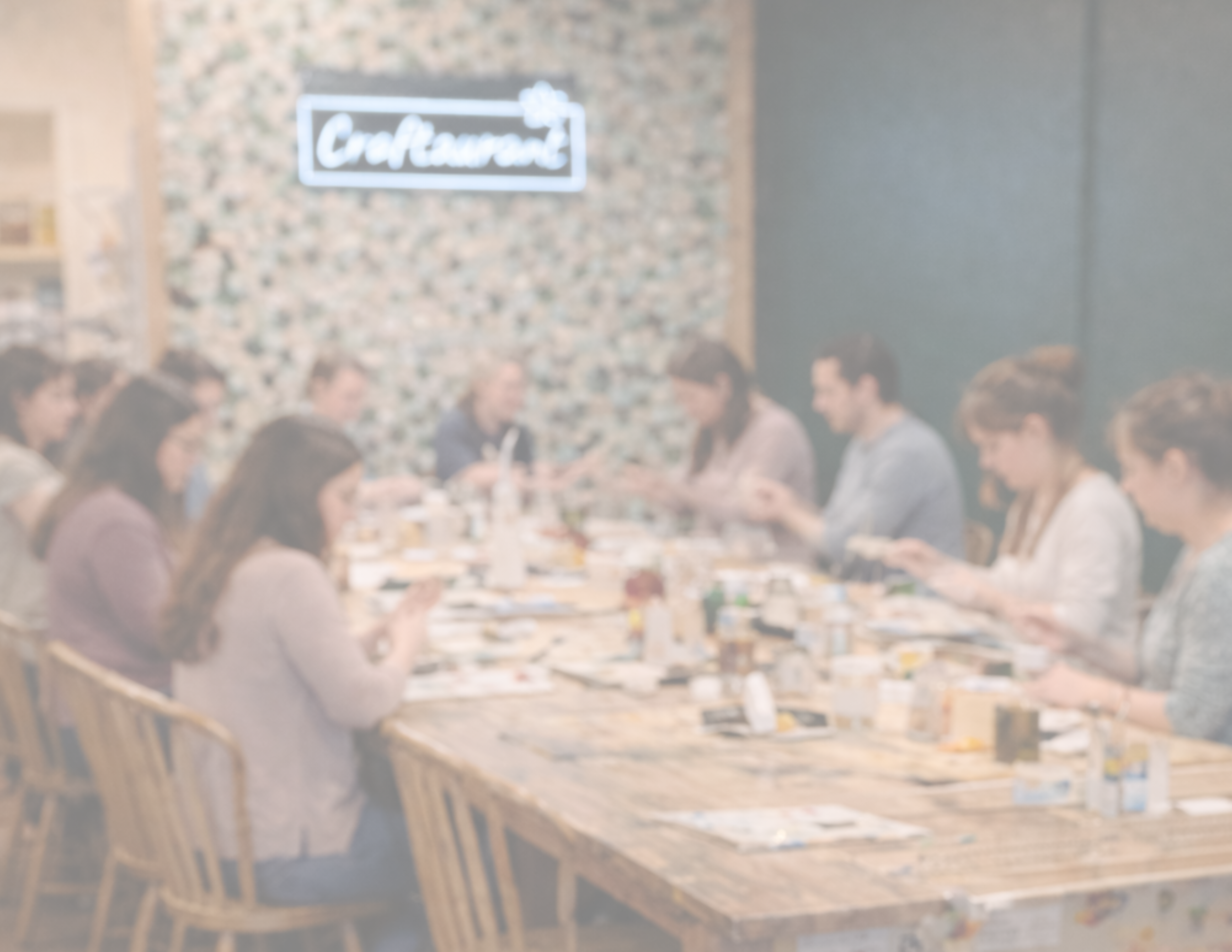 Group of people sitting around a long wooden table in a restaurant with 'Craftaurant' sign in the background.