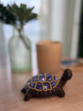 Decorative turtle figurine with blue and gold embellishments on a wooden surface.