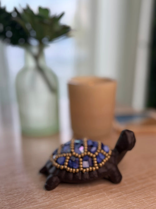 Decorative turtle figurine with blue and gold embellishments on a wooden surface.